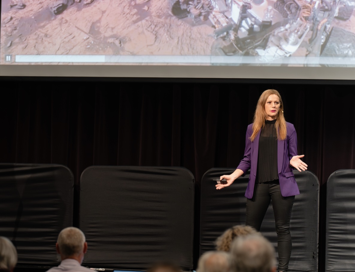 Rebecca Maklad delivering a keynote in a purple blazer on stage